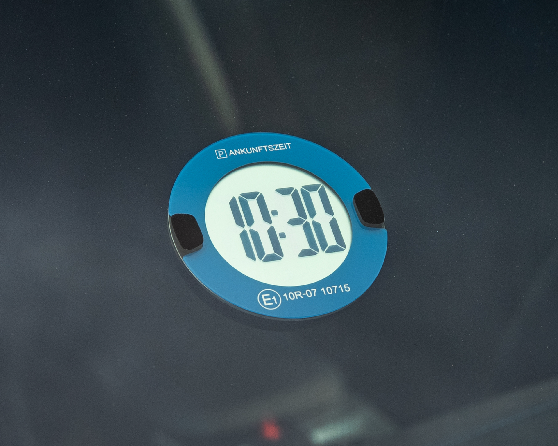 An der Windschutzscheibe eines Autos sind eine blau-weiße Parkscheibe und ein Verkehrsalarm angebracht, der die Uhrzeit 8:30 anzeigt.