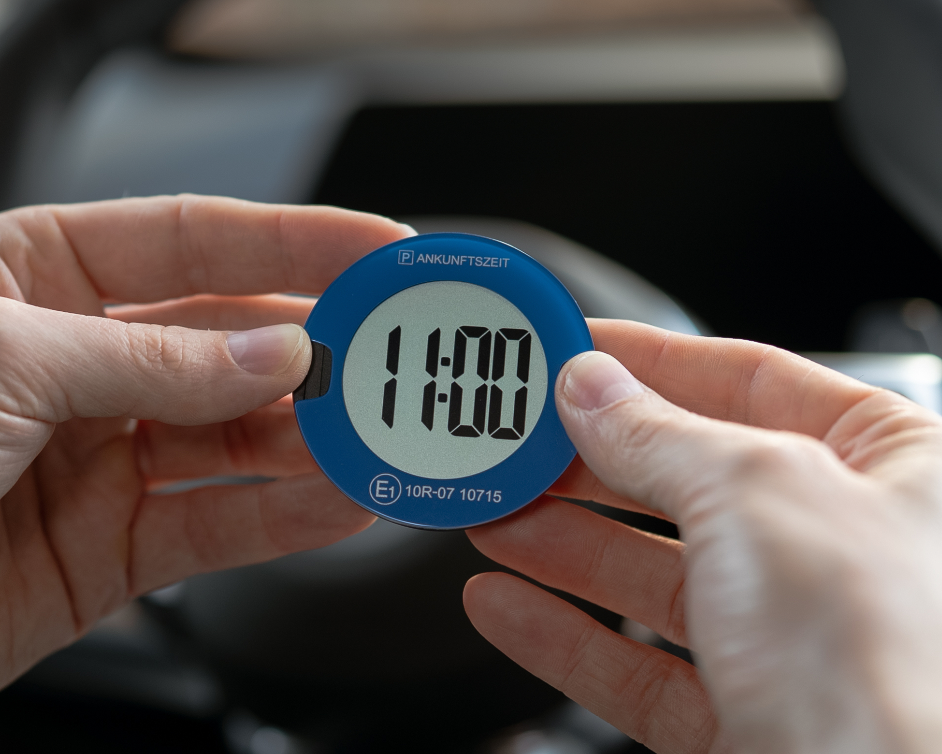Person, die eine blaue digitale Parkscheibe und einen Trafikalarm in einem Auto hält, das Display zeigt 14:00 an, und das Produkt beim Parken benutzt.